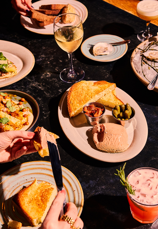 A table set with plates of grilled cheese, a side salad, pickles, and a glass of wine.