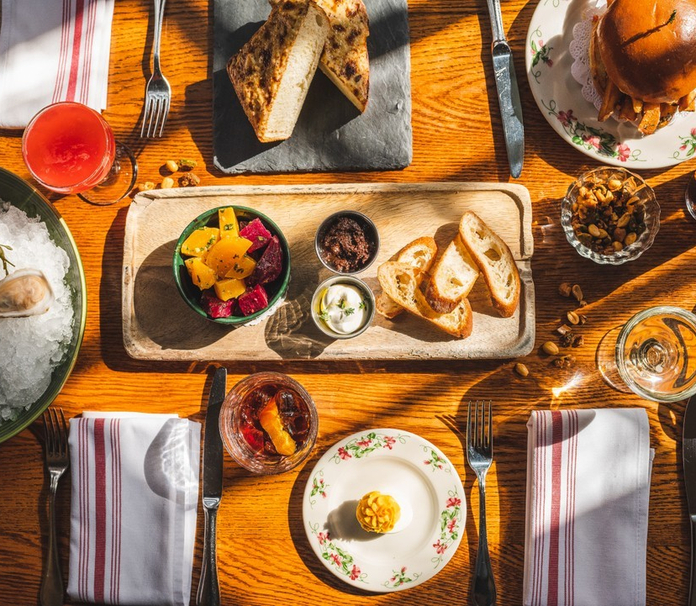 A warmly lit restaurant table set for a meal, featuring oysters, bread, a burger, and assorted sauces.