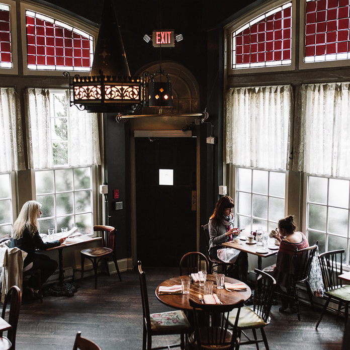 Warm, cozy restaurant with large windows, tables, and patrons enjoying meals. Dark walls and red-tiled ceiling.