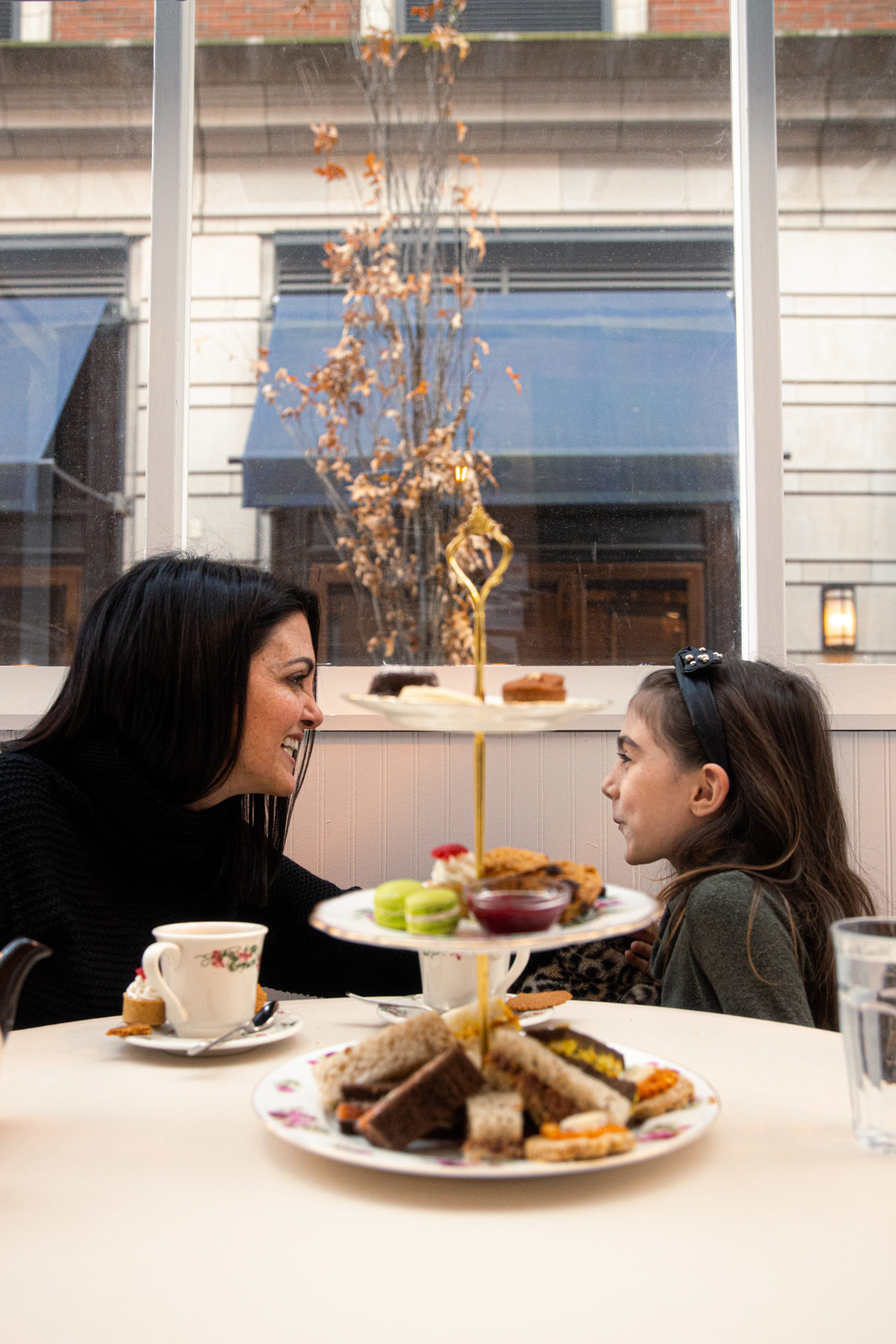 Mother and daughter enjoying afternoon tea - stacked cake plate with little sandwiches and desserts